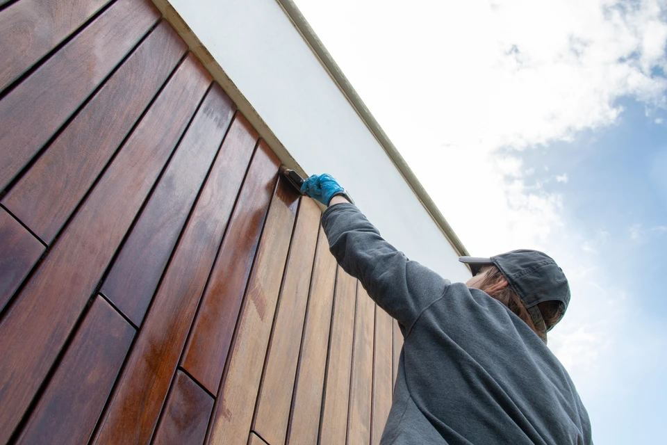 Ouvrier en gants bleus appliquant un traitement sur bardage bois extérieur d'un bâtiment moderne
