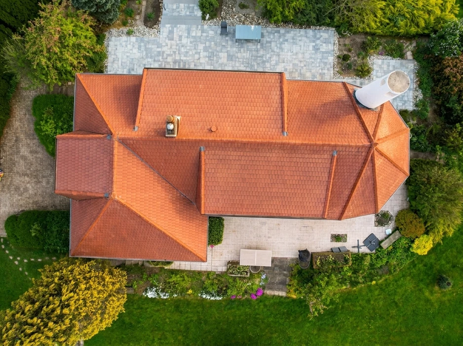 Vue aérienne par drone d'une grande maison individuelle avec toiture complexe en tuiles terre cuite, configuration en croupe et noues métalliques apparentes
