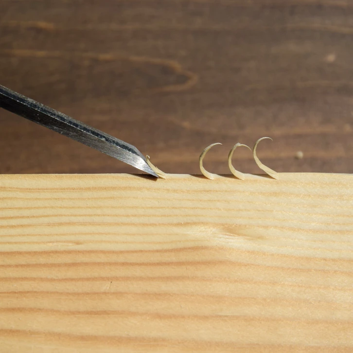 Atelier de menuiserie avec ciseau à bois en action sur planche de pin, produisant des copeaux fins et réguliers