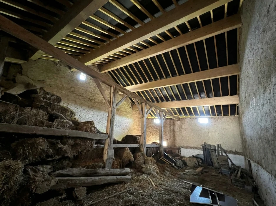 Intérieur d'une grange ancienne en pierre, avec charpente en bois apparente composée de chevrons et pannes