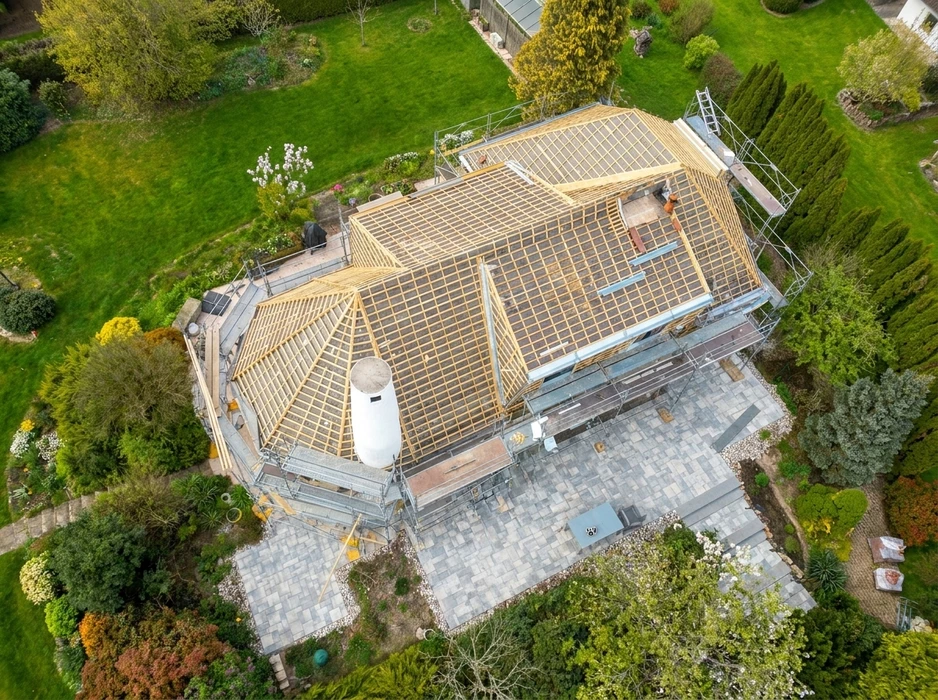 Vue aérienne par drone d'une grande maison individuelle avec toiture complexe en tuiles terre cuite, configuration en croupe et noues métalliques apparentes